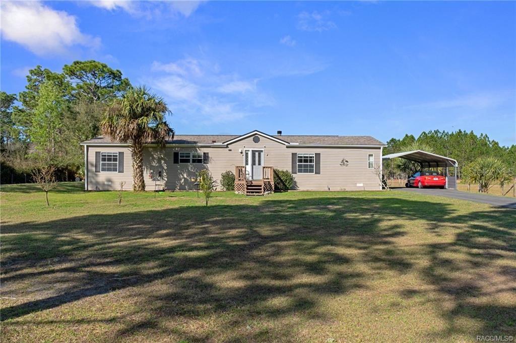 A single-story manufactured home with light siding, a front porch, and a detached carport — 2430 S WAKULLA POINT, HOMOSASSA, FL
