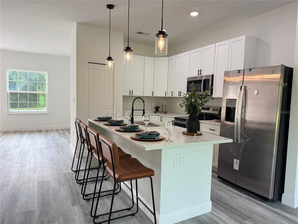 A modern kitchen features white cabinets, a quartz island with bar seating, and stainless appliances — 3901 SW 161ST LOOP, OCALA, FL