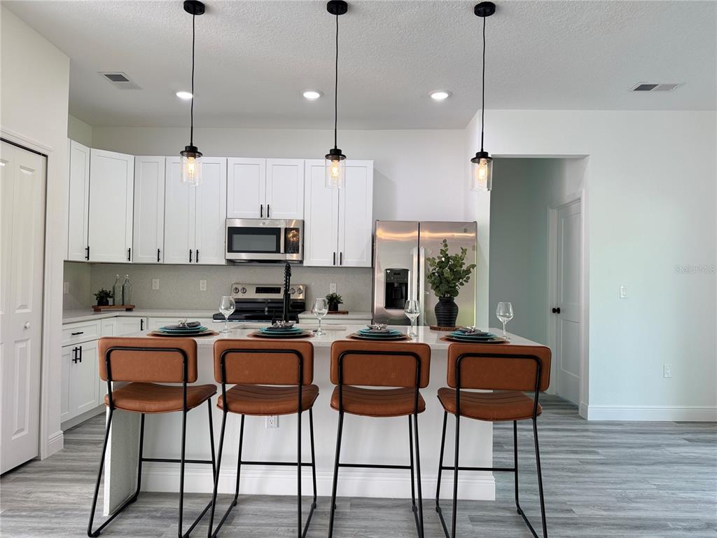 A kitchen features white cabinets, a quartz island with bar seating, and stainless steel appliances — 3901 SW 161ST LOOP, OCALA, FL