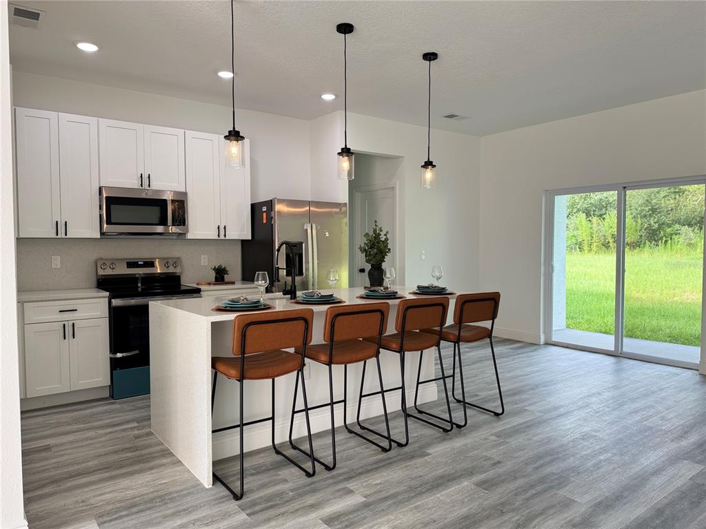 A modern kitchen features white cabinets, stainless steel appliances, a breakfast bar, and four stools — 3901 SW 161ST LOOP, OCALA, FL