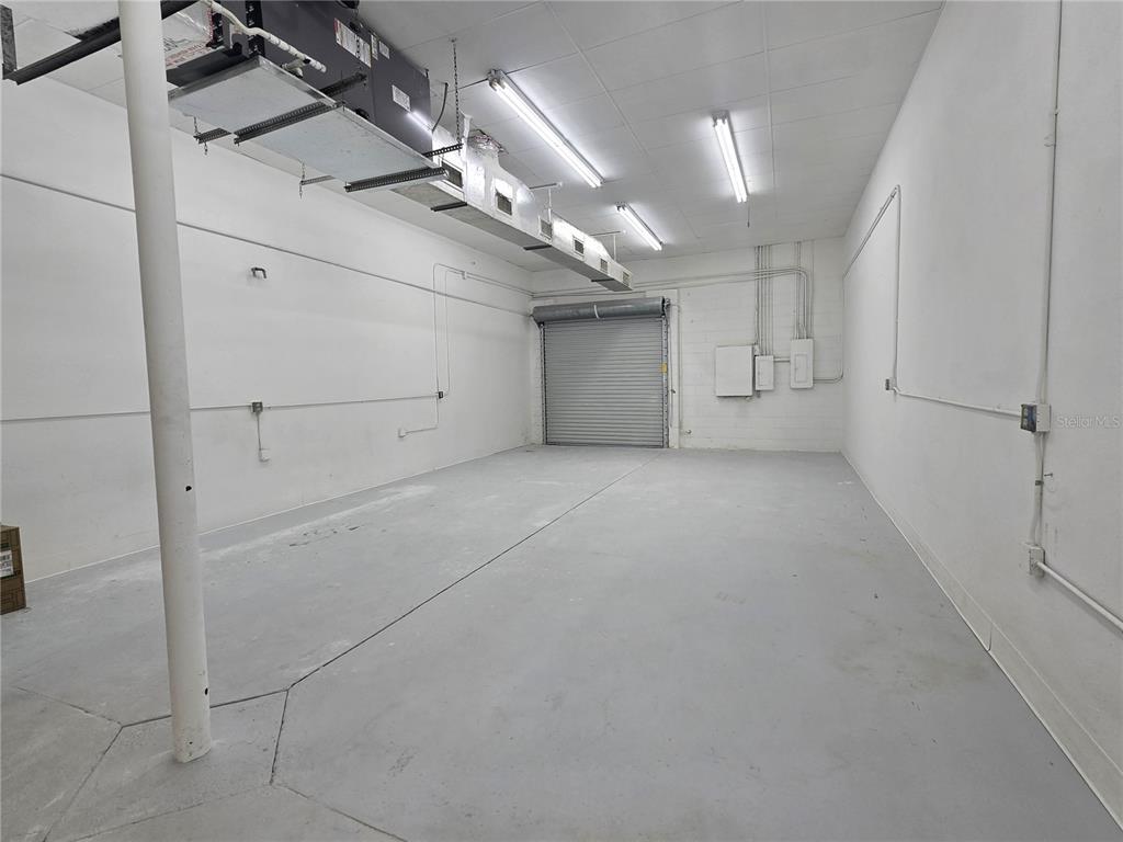 An empty industrial storage unit with a roll-up door, exposed ductwork, and concrete floors — 9225 ULMERTON ROAD UNIT N, LARGO, FL
