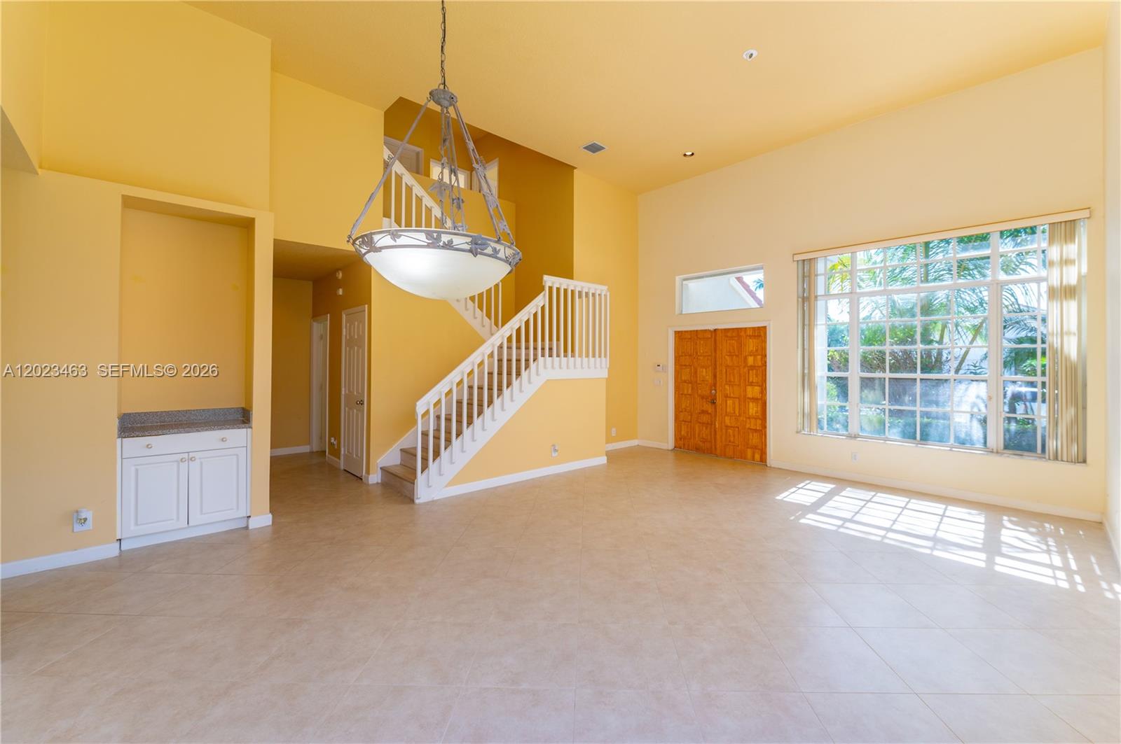 A spacious, yellow-walled foyer features a large chandelier, a staircase, and tile flooring — 7131 NW Turtle Walk, Boca Raton FL 33487, BOCA RATON, FL