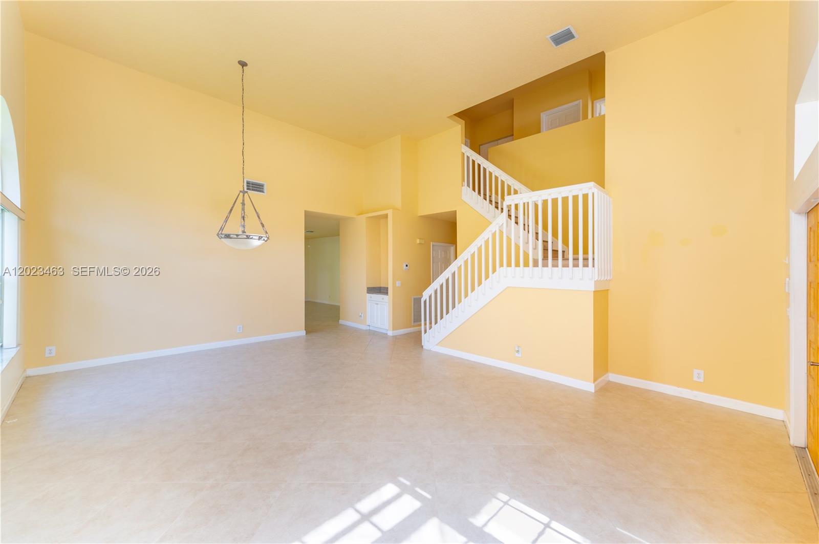 A spacious room with yellow walls, tile flooring, and a staircase with white railings — 7131 NW Turtle Walk, Boca Raton FL 33487, BOCA RATON, FL