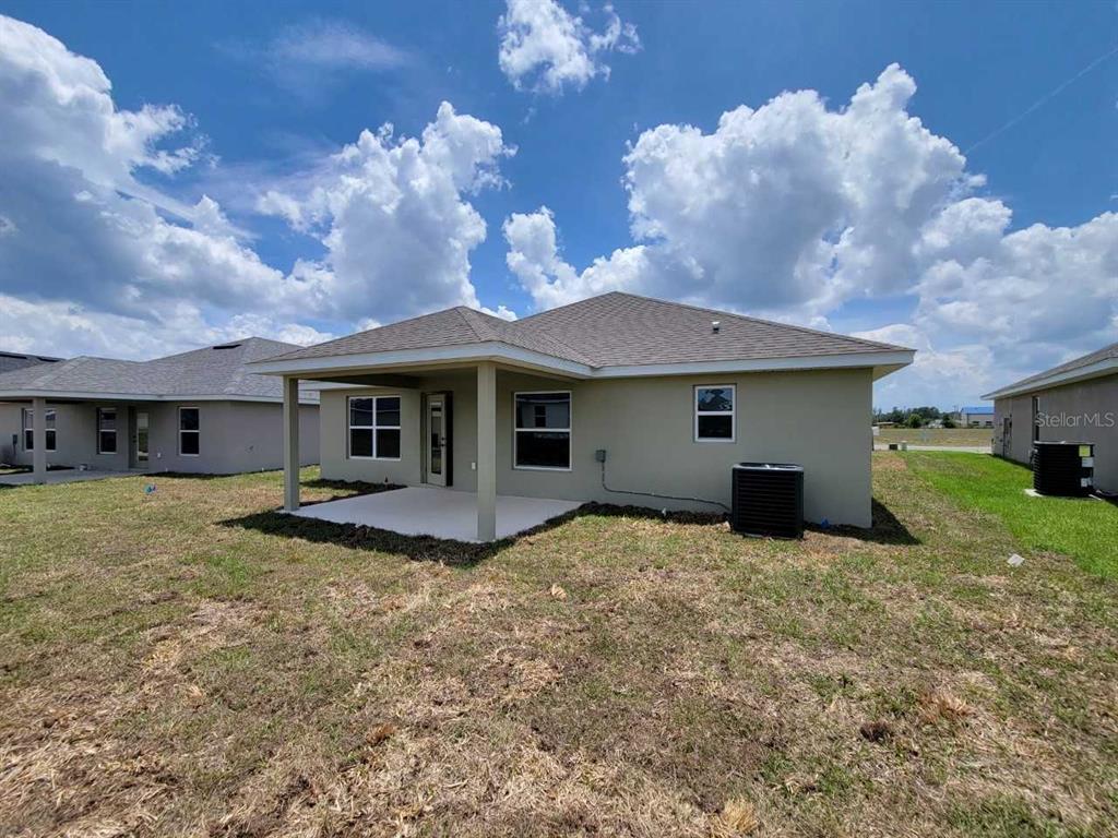 The back exterior of a tan house features a covered patio and a central air unit — 4392 SW 92ND PLACE ROAD, OCALA, FL