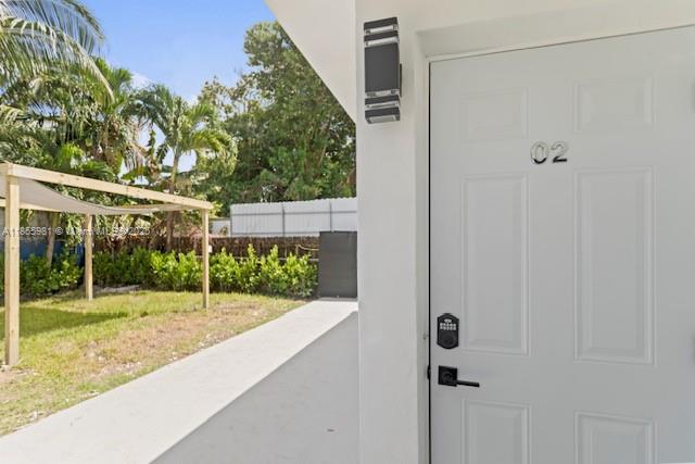 A white door labeled 02 opens to a concrete walkway beside a grassy yard with landscaping — 3125 NW 21st Ct # 02, Miami FL 33142, MIAMI, FL