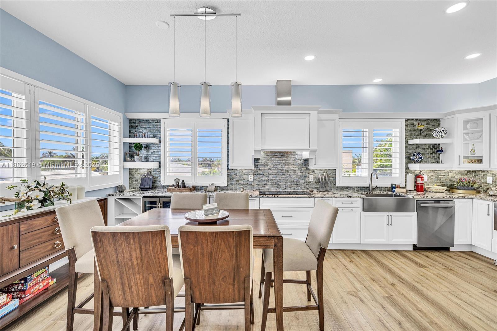 A kitchen features white cabinetry, a wooden dining table, and blue walls with plantation shutters — 311 N Surf Rd # 311, Hollywood FL 33019, HOLLYWOOD, FL