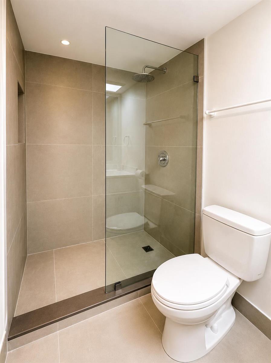 A bathroom features a walk-in shower with a glass panel, beige tile, and a toilet — 4200 Oaks Terrace # 104, Pompano Beach FL 33069, POMPANO BEACH, FL