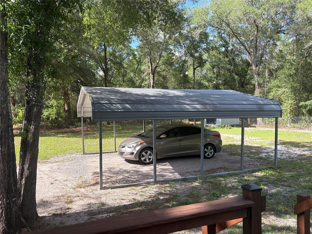 A metal carport shelters a tan sedan on a gravel driveway surrounded by trees — 15210 NE 144TH STREET, FORT MC COY, FL