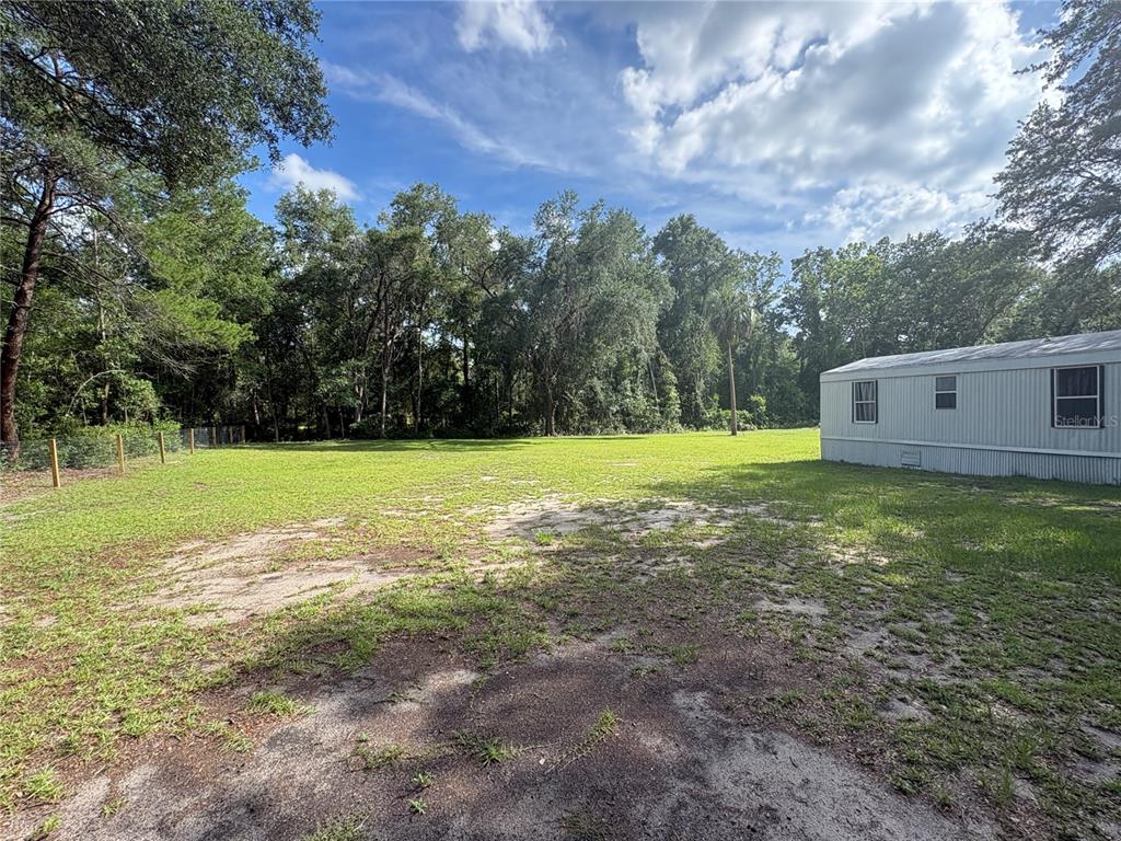 A grassy yard features a mobile home on the right and a wooded backdrop — 15210 NE 144TH STREET, FORT MC COY, FL