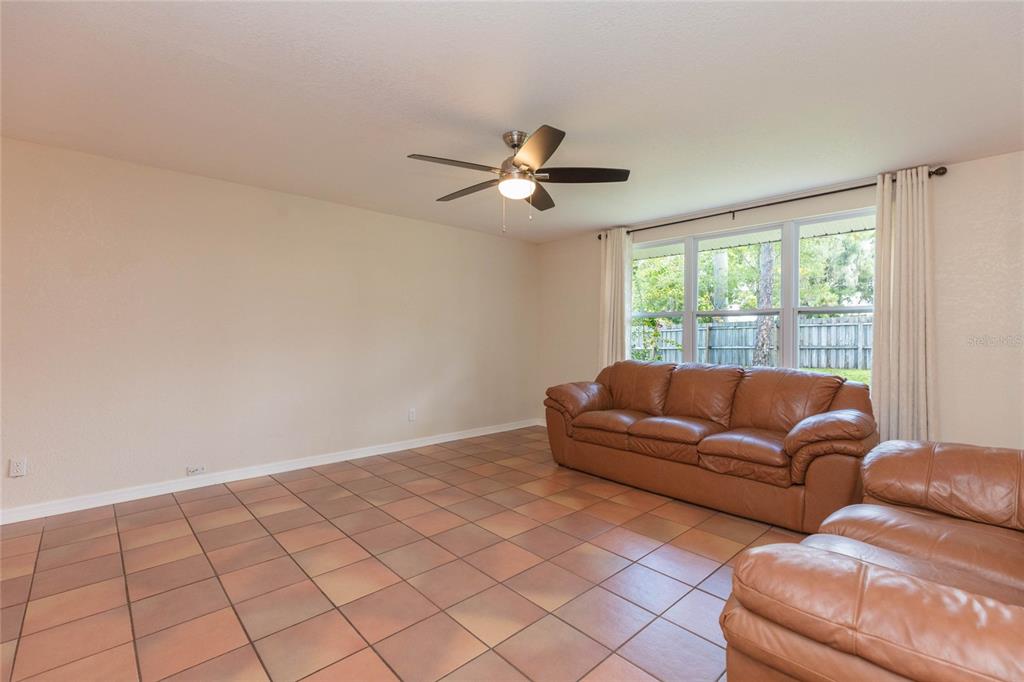 A living room with tan tile flooring, a ceiling fan, and a brown leather sofa — 8719 HANDCART ROAD, WESLEY CHAPEL, FL