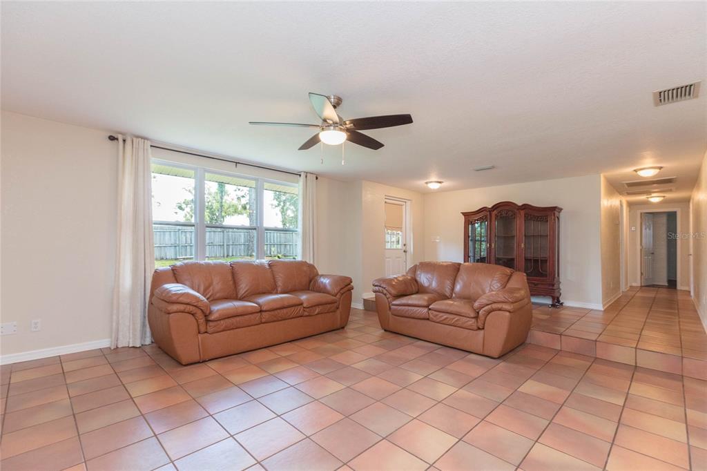 A living room with tan tile floors, two brown leather sofas, and a ceiling fan — 8719 HANDCART ROAD, WESLEY CHAPEL, FL