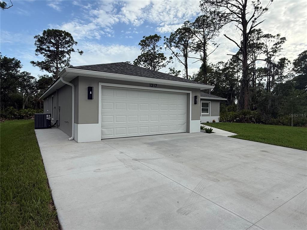 A gray house with a white garage door and a concrete driveway sits among trees — 1317 BISCAYNE DRIVE, PORT CHARLOTTE, FL