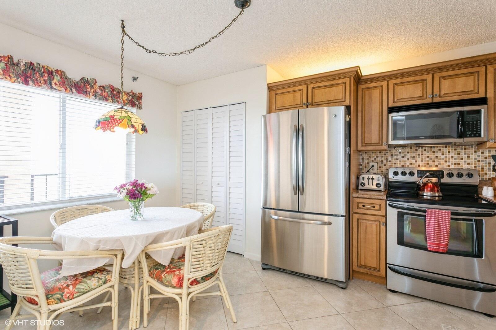 A kitchen features stainless steel appliances, wood cabinets, and a small dining area with wicker chairs — 275 Palm Avenue # B403, Jupiter FL 33477, JUPITER, FL