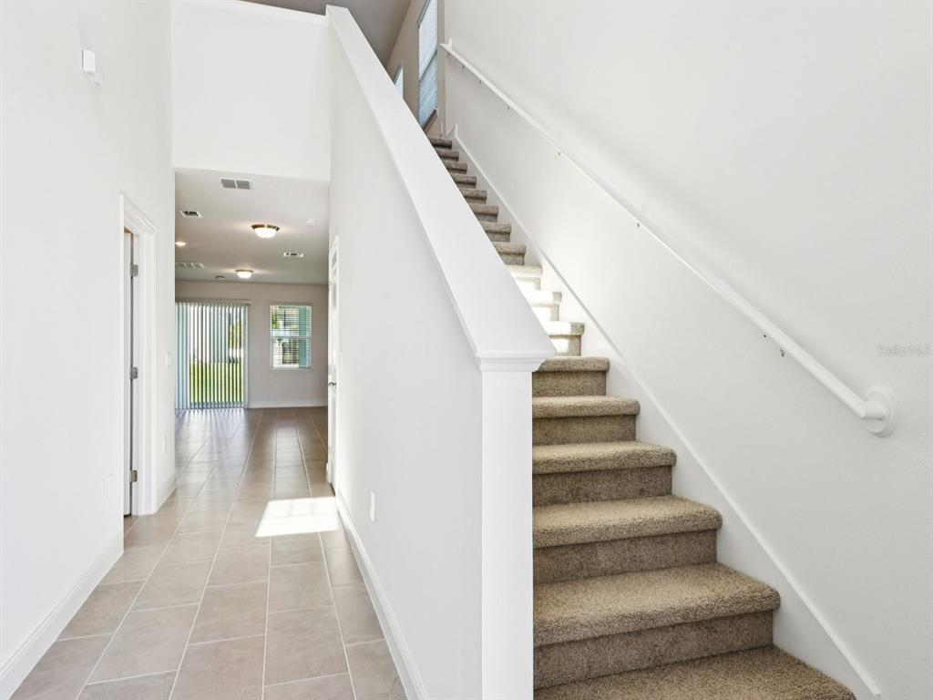 A carpeted staircase with a white railing sits beside a tiled hallway leading to a room — 2186 WILDBERRY WAY, MINNEOLA, FL