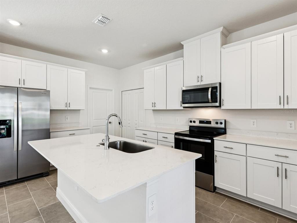 A kitchen with white cabinets, stainless steel appliances, a center island, and light-colored countertops — 2186 WILDBERRY WAY, MINNEOLA, FL