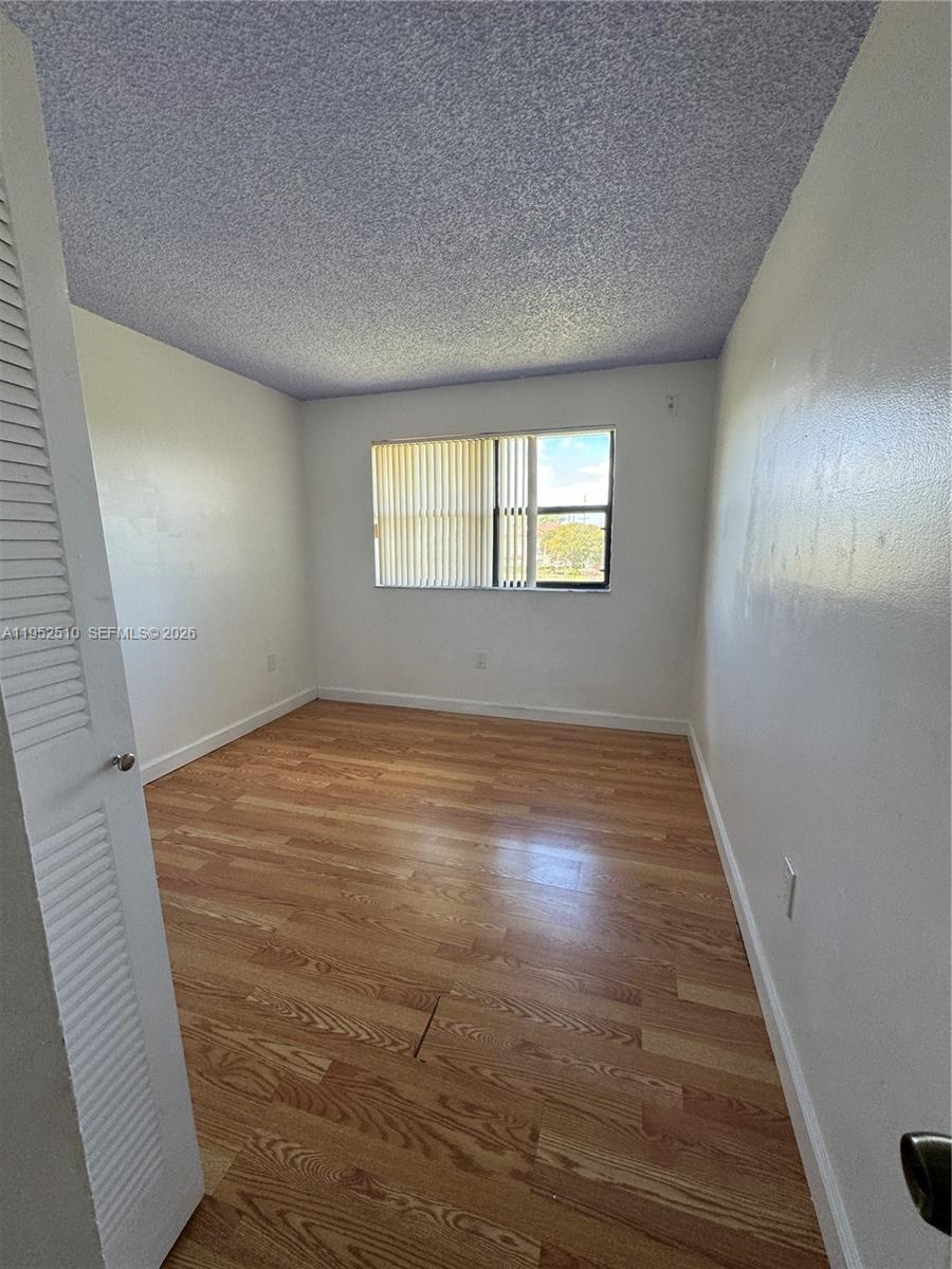 An empty bedroom features light wood-look flooring, white walls, and a textured ceiling — 7235 NW 179th St # 311, Hialeah FL 33015, HIALEAH, FL