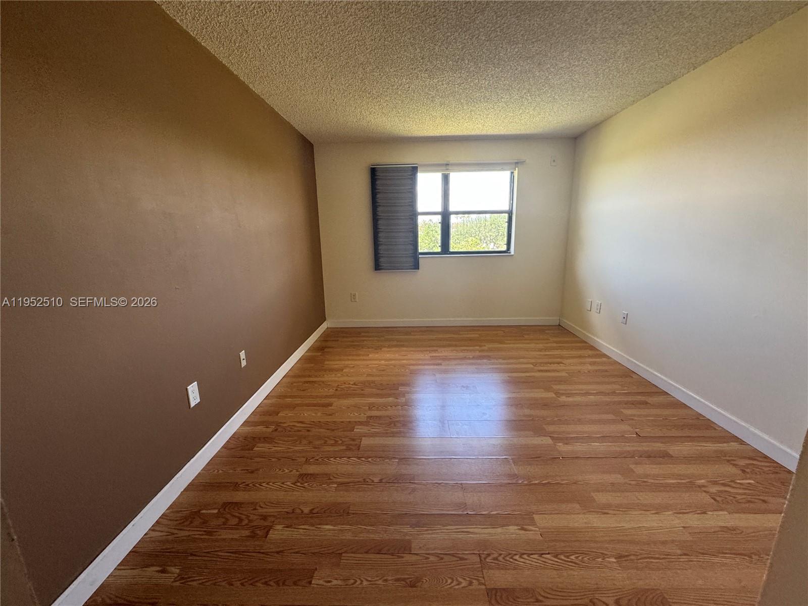 An empty room features wood-look flooring, a brown accent wall, and a single window — 7235 NW 179th St # 311, Hialeah FL 33015, HIALEAH, FL
