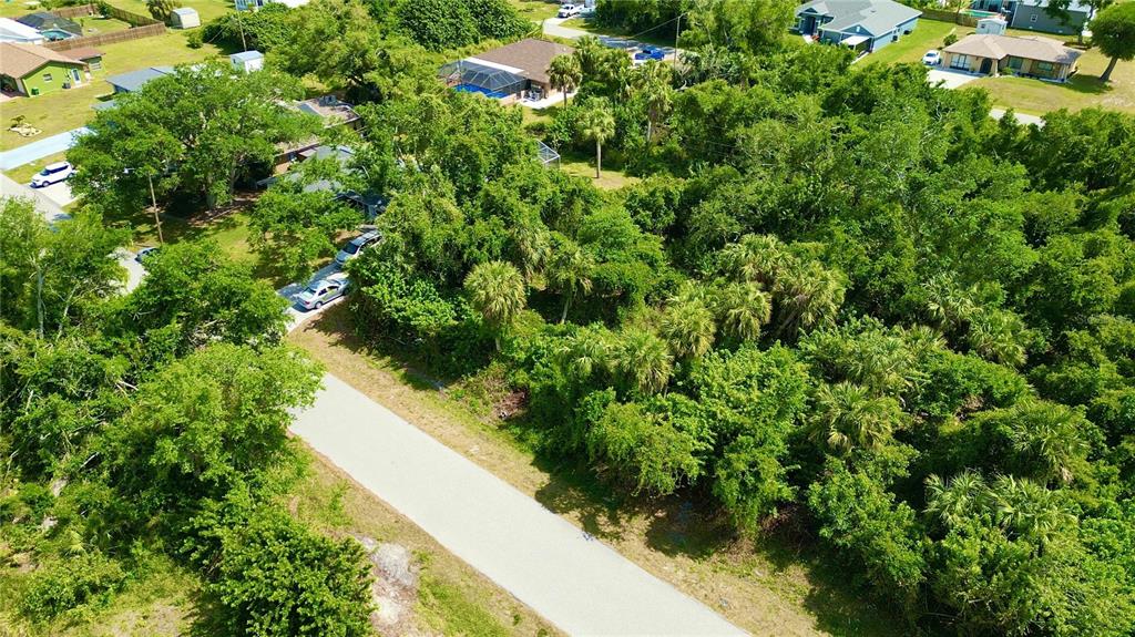 An aerial view shows a paved road leading toward a dense, wooded residential lot — 1181 BELMAR AVENUE, PORT CHARLOTTE, FL