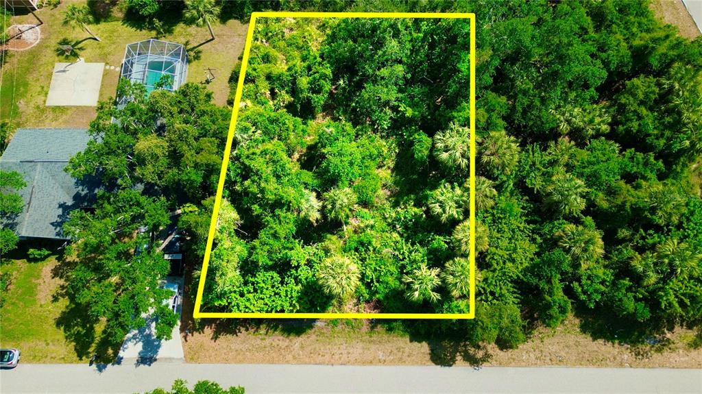 An aerial view shows a rectangular, tree-covered vacant lot outlined in yellow next to a house — 1181 BELMAR AVENUE, PORT CHARLOTTE, FL