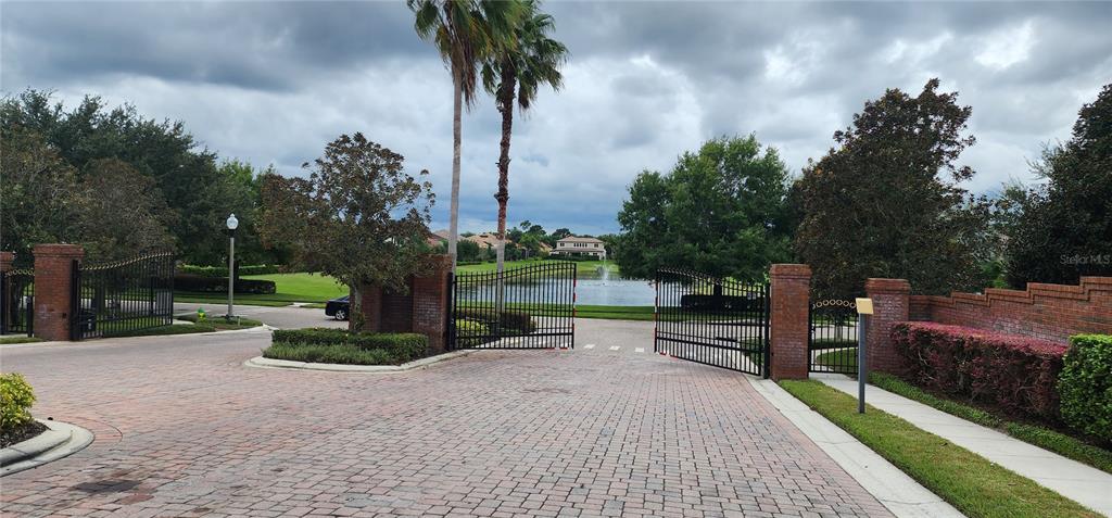A gated entrance with brick pillars leads to a paved driveway and a small lake — 1198 BELLA VISTA CIR, LONGWOOD, FL