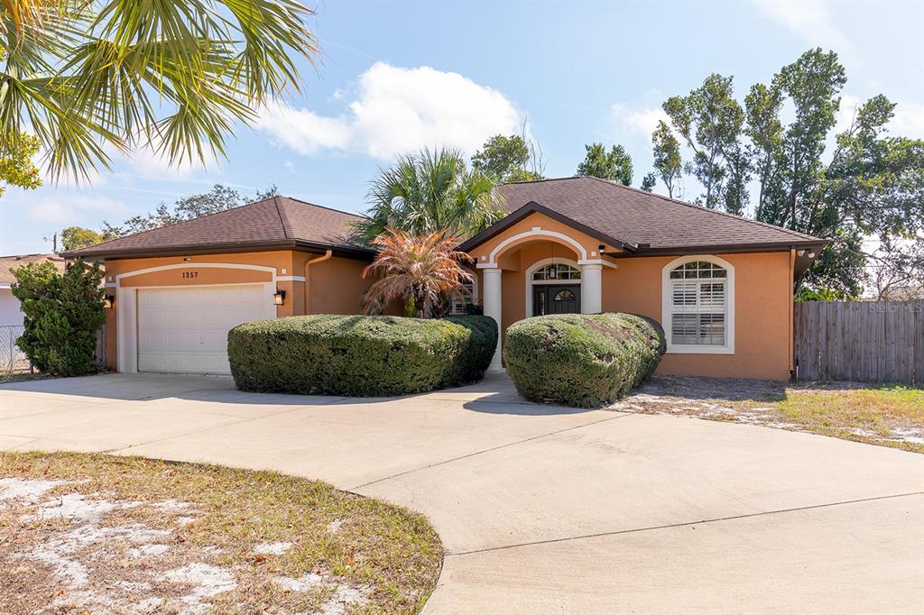A single-story house with a tan stucco exterior, a two-car garage, and manicured landscaping — 1357 PROVIDENCE BOULEVARD, DELTONA, FL