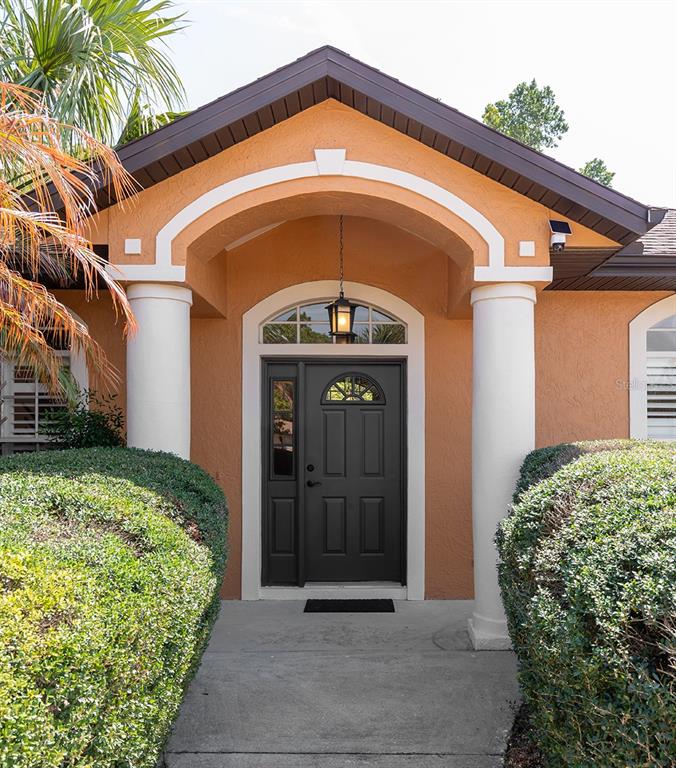 The front entrance of a house features a dark door, white columns, and arched trim — 1357 PROVIDENCE BOULEVARD, DELTONA, FL