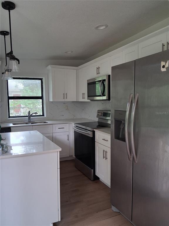 A kitchen features white cabinets, stainless steel appliances, a kitchen island, and light wood flooring — 2713 BERDETTA STREET, LEESBURG, FL