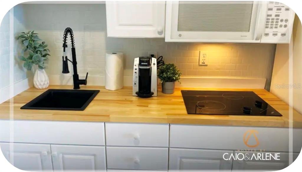 A kitchen features white cabinets, a light wood countertop, a black sink, and a stovetop — 2700 N ATLANTIC AVENUE UNIT 915, DAYTONA BEACH, FL