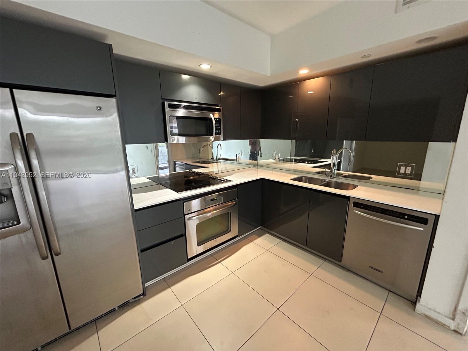 A modern kitchen features dark gray cabinetry, stainless steel appliances, and a mirrored backsplash — 31 SE 6th St # 407, Miami FL 33131, MIAMI, FL