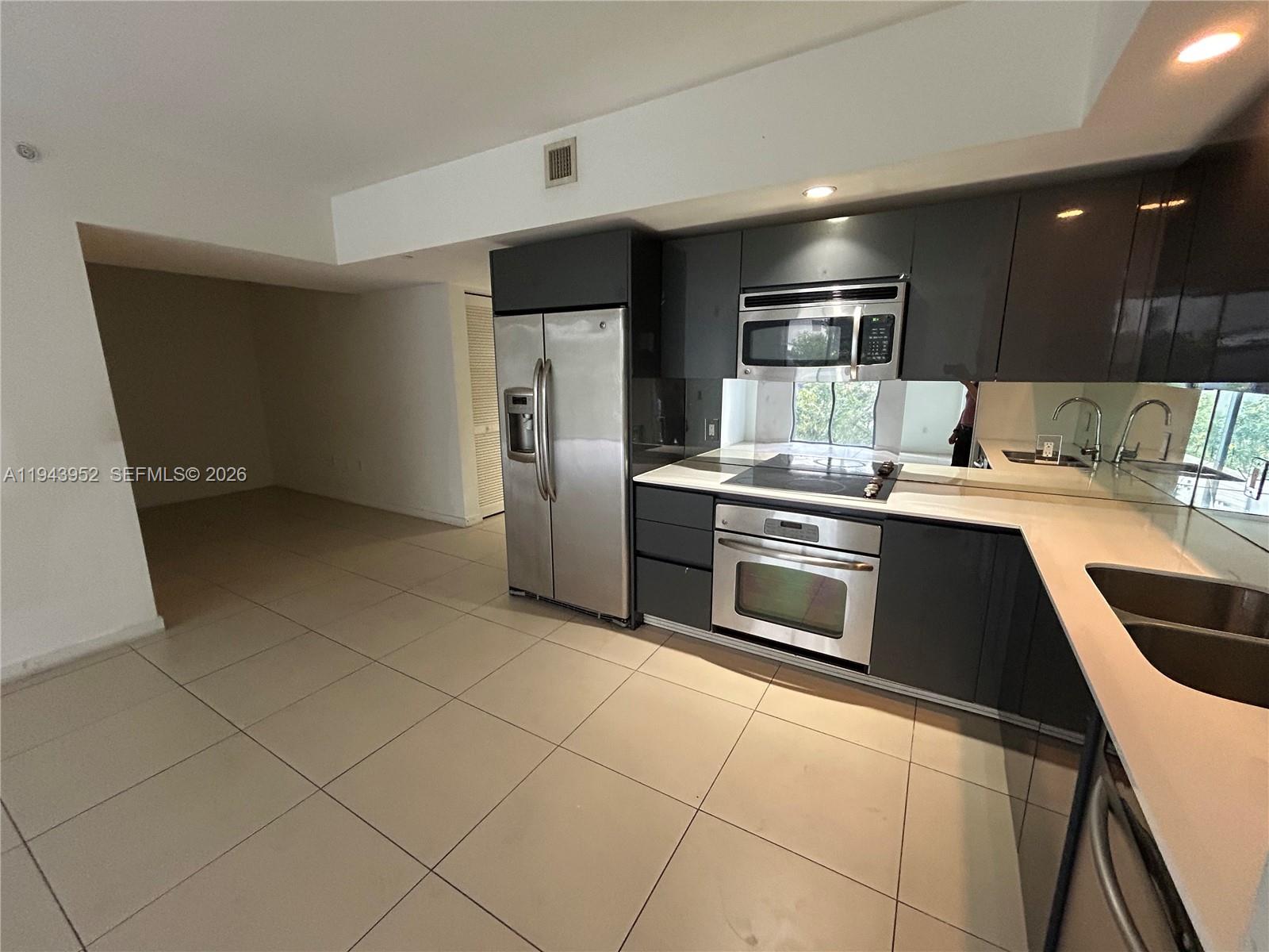 A modern kitchen features dark gray cabinetry, stainless steel appliances, and light-colored tile flooring — 31 SE 6th St # 407, Miami FL 33131, MIAMI, FL