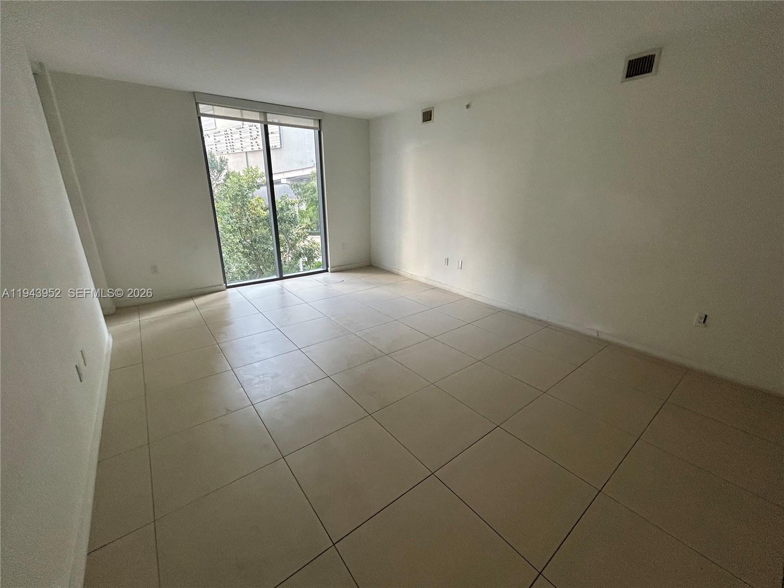 An empty room features large light-colored floor tiles, white walls, and a floor-to-ceiling window — 31 SE 6th St # 407, Miami FL 33131, MIAMI, FL