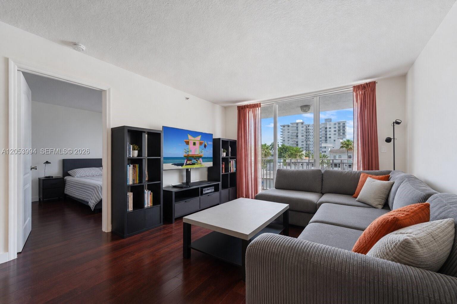 A living room with a grey sectional sofa, media console, and view of city buildings — 2642 Collins Ave # 303, Miami Beach FL 33140, MIAMI BEACH, FL