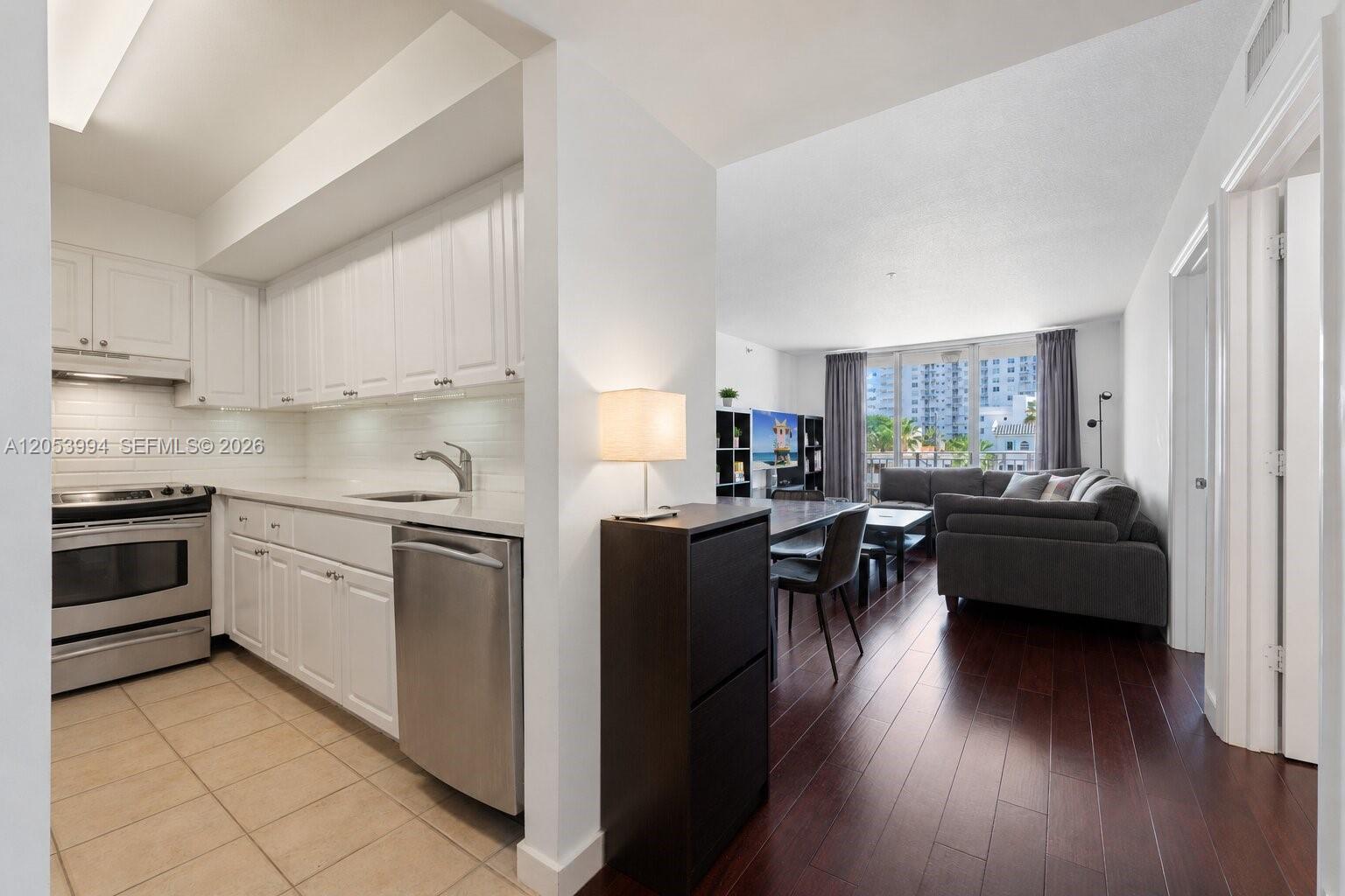 A kitchen with white cabinets and tile floors opens into a living area with hardwood — 2642 Collins Ave # 303, Miami Beach FL 33140, MIAMI BEACH, FL