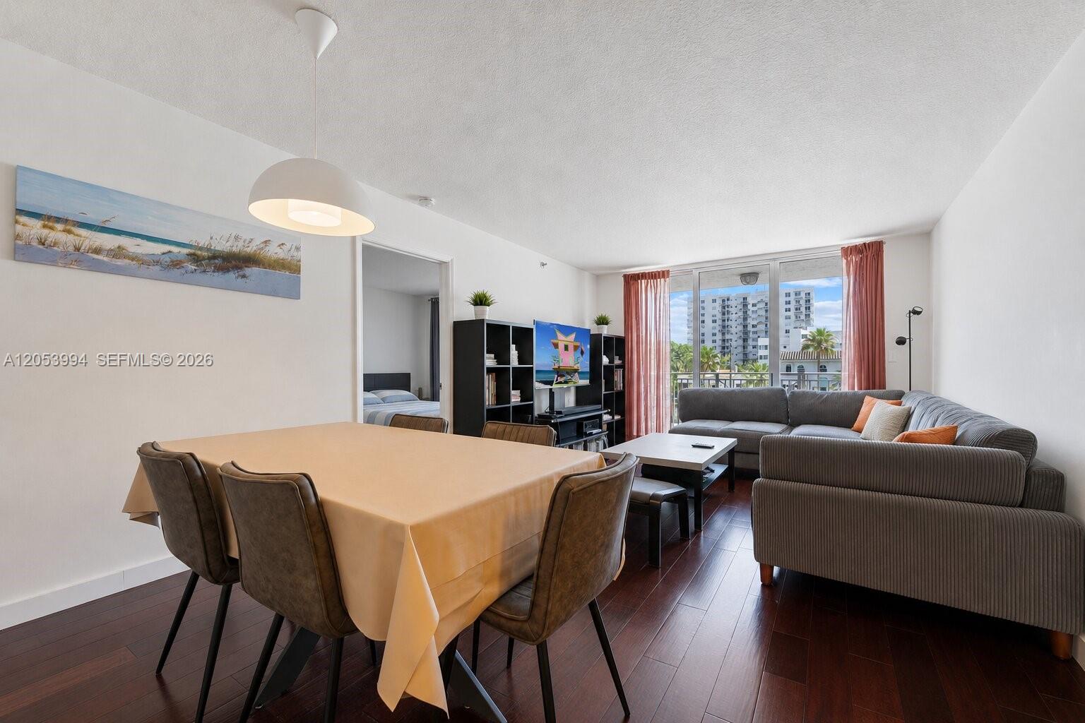 A living and dining area features dark wood floors, a gray sectional, and balcony access — 2642 Collins Ave # 303, Miami Beach FL 33140, MIAMI BEACH, FL