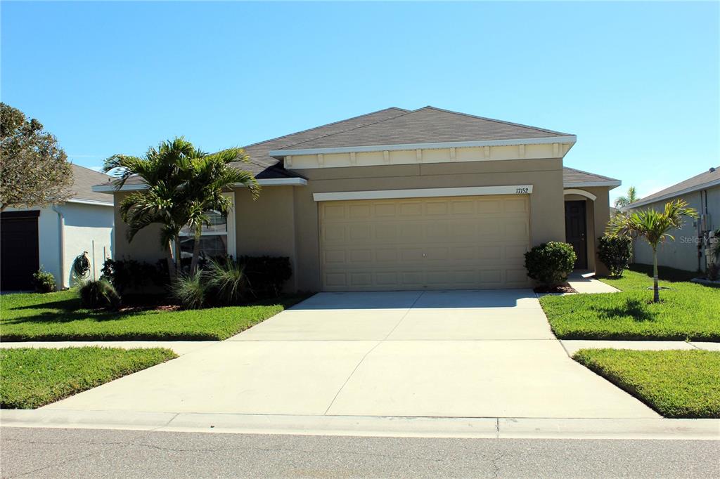 A single-story house with a beige stucco exterior, a two-car garage, and a concrete driveway — 17152 SUNSHINE MIMOSA STREET, WIMAUMA, FL