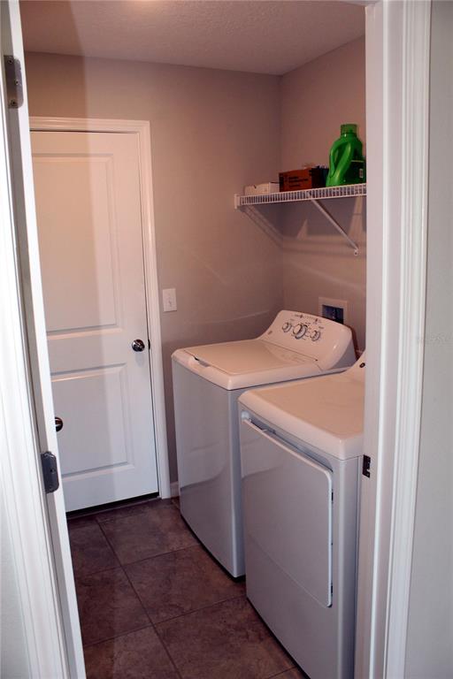 A laundry room features a white washer and dryer, tile flooring, and a wire wall shelf — 17152 SUNSHINE MIMOSA STREET, WIMAUMA, FL