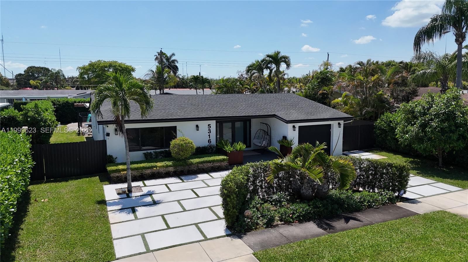A single-story white house with a dark roof, paved driveway, and lush tropical landscaping — 5316 Jackson St, Hollywood FL 33021, HOLLYWOOD, FL