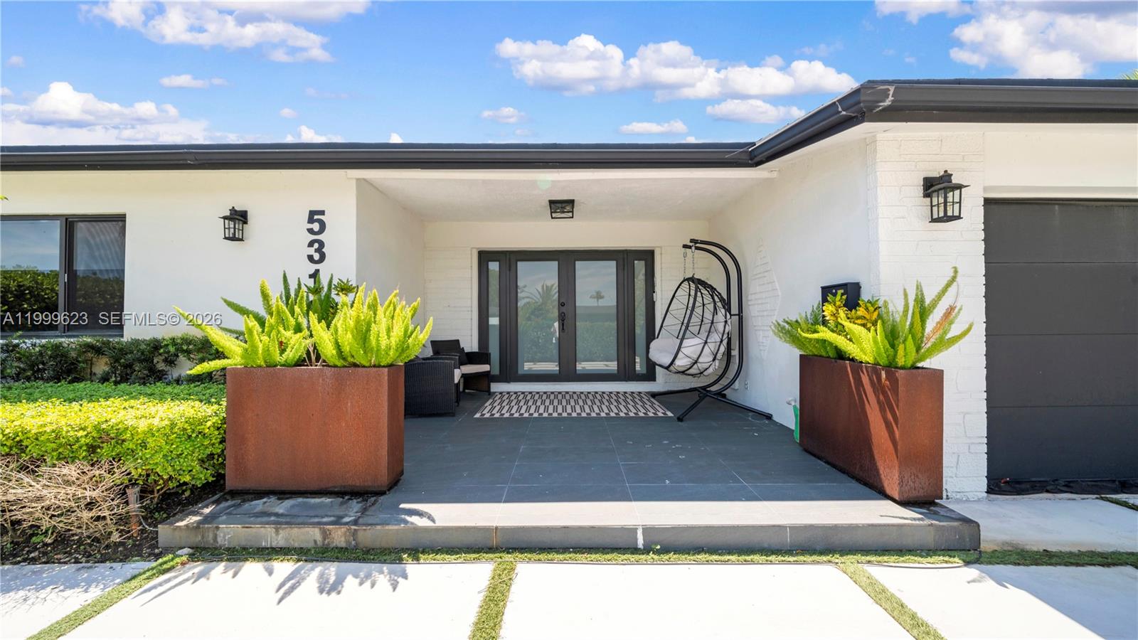 A modern home entrance features a covered porch, dark double doors, and two large planters — 5316 Jackson St, Hollywood FL 33021, HOLLYWOOD, FL