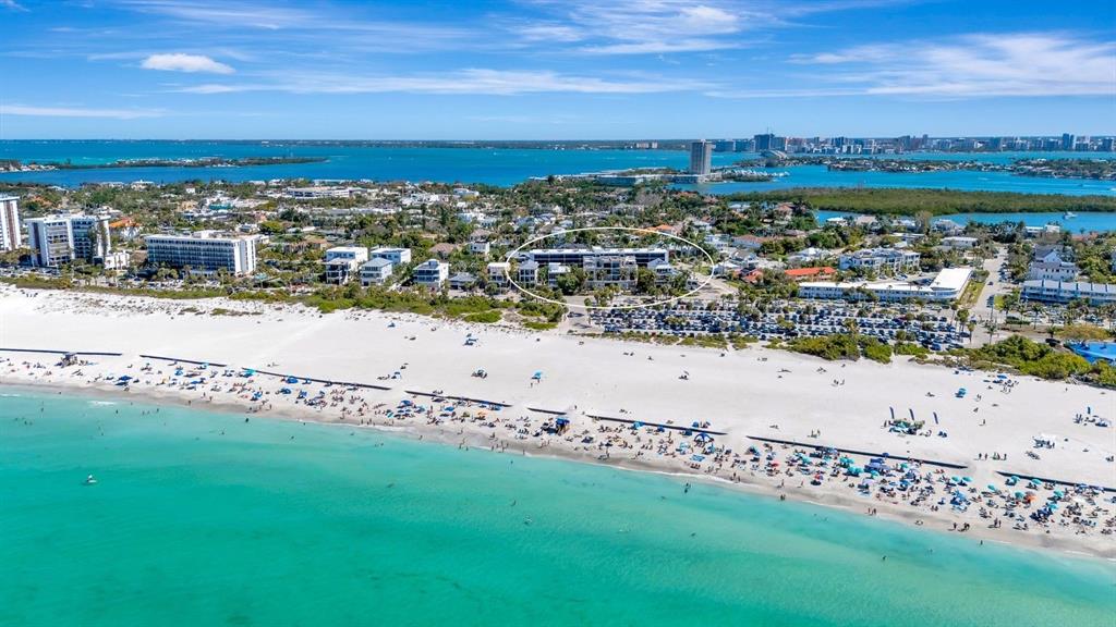 An aerial view shows a beach with many people, surrounding buildings, and a circled resort — 350 S POLK DRIVE UNIT 302, SARASOTA, FL