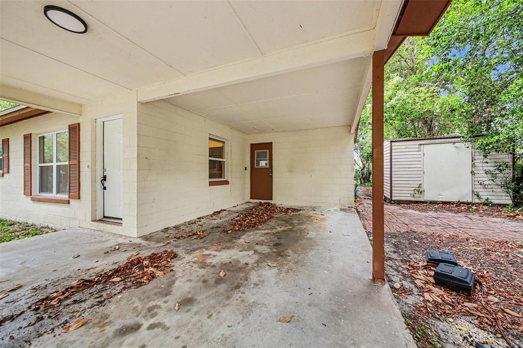A concrete carport with a brown door, a window, and a detached shed in the background — 2318 JOBBINS DRIVE, LEESBURG, FL