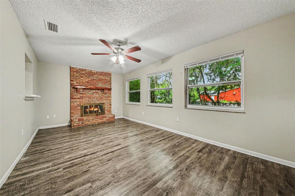 A living room with wood-look flooring, a brick fireplace, and three windows — 2318 JOBBINS DRIVE, LEESBURG, FL