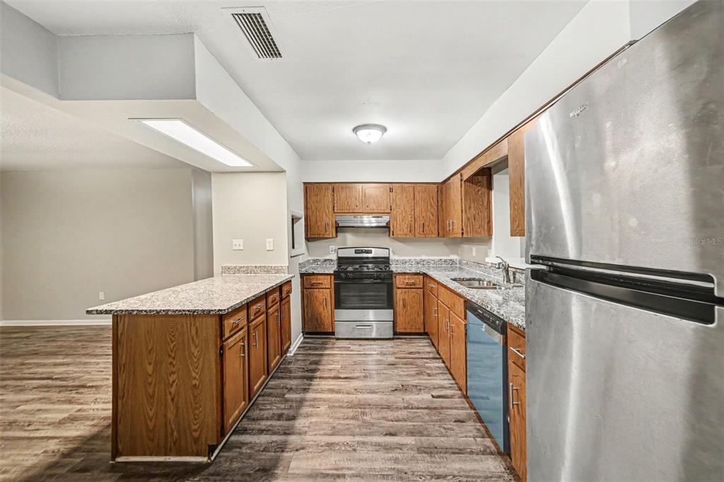 A kitchen features wood cabinets, granite countertops, stainless steel appliances, and wood-look flooring — 2318 JOBBINS DRIVE, LEESBURG, FL