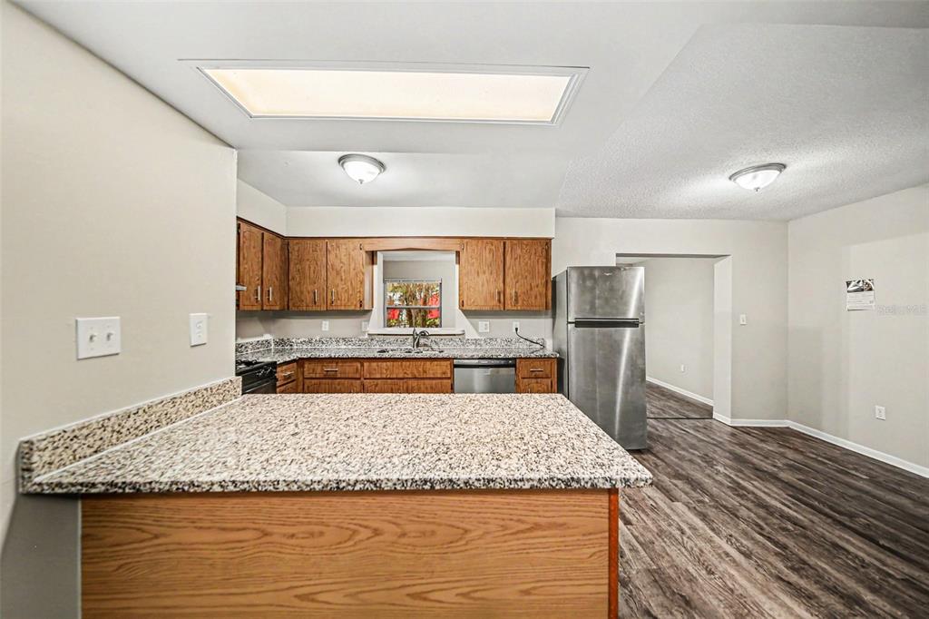 A kitchen features wood cabinets, granite countertops, stainless steel appliances, and wood-look flooring — 2318 JOBBINS DRIVE, LEESBURG, FL