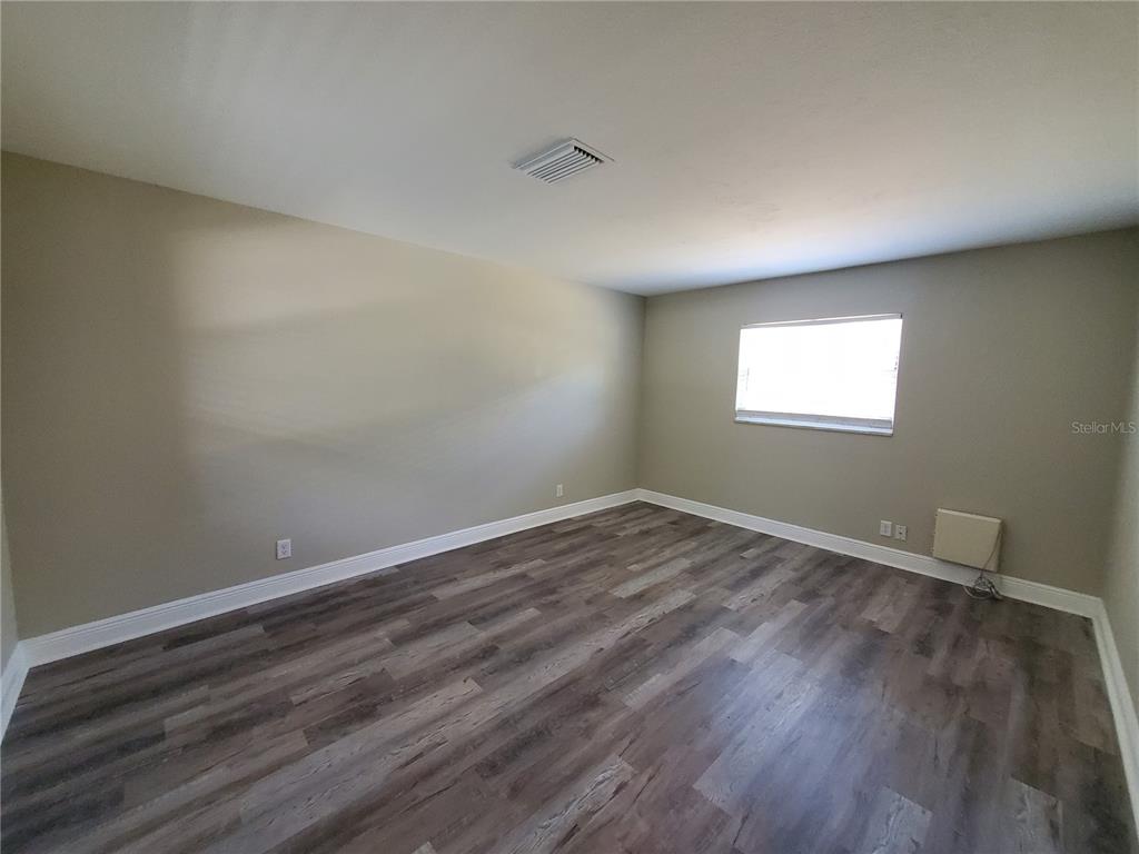 An empty room features light-colored walls, gray wood-look flooring, a window, and a wall-mounted unit — 107 W CLAY AVENUE UNIT 4, BRANDON, FL