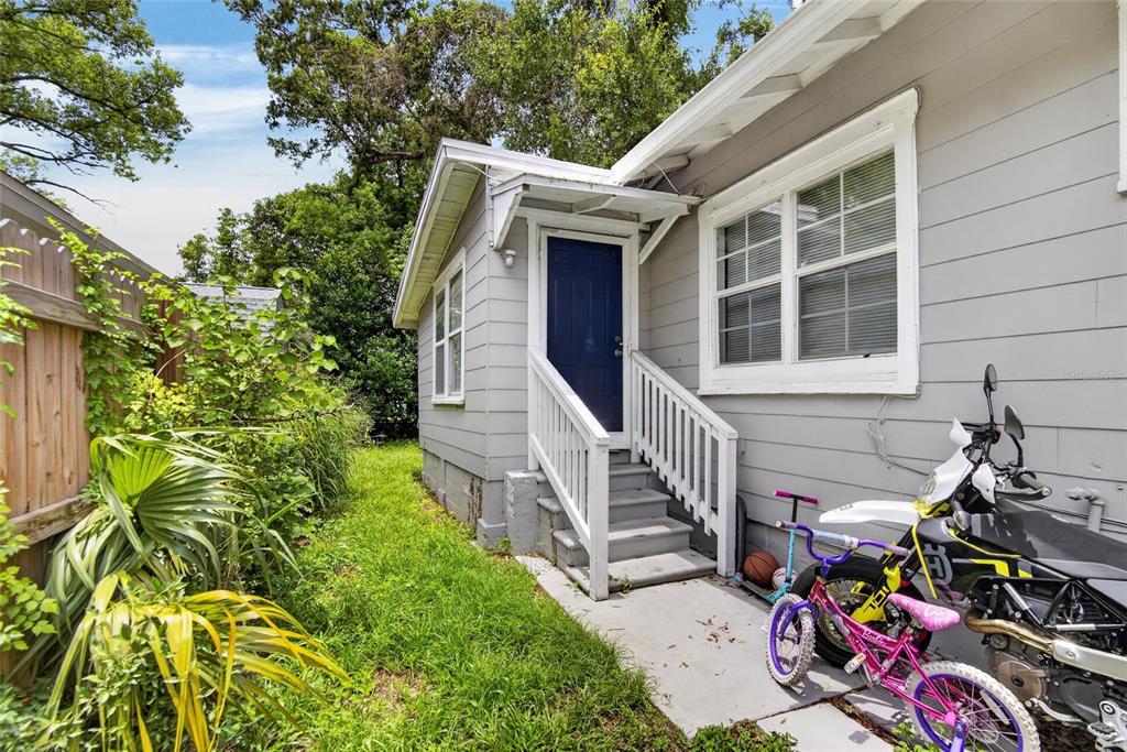 A gray house exterior features a blue door, white stairs, and a concrete walkway — 8114 N 11TH STREET, TAMPA, FL