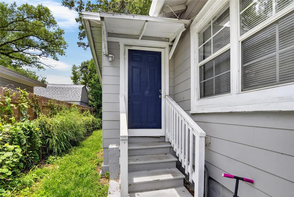 A blue door with a small awning and wooden stairs sits on the side exterior — 8114 N 11TH STREET, TAMPA, FL