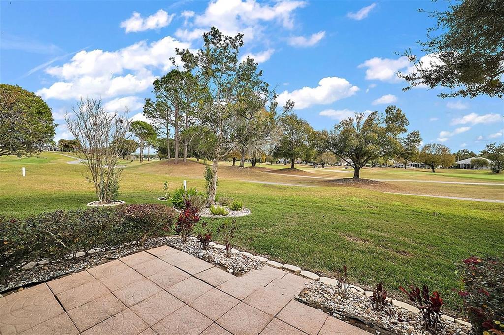 A paved patio overlooks a grassy golf course with scattered trees under a blue sky — 13667 SE 91ST AVENUE, SUMMERFIELD, FL