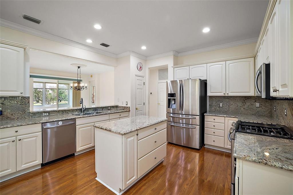 A kitchen features white cabinets, granite countertops, stainless steel appliances, and hardwood flooring — 13667 SE 91ST AVENUE, SUMMERFIELD, FL