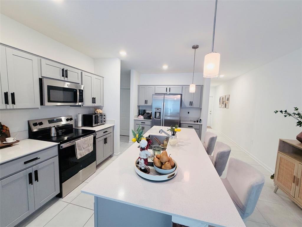 A modern kitchen features gray cabinets, stainless steel appliances, and a large white quartz island — 2715 GENTLE RAIN DRIVE, DAVENPORT, FL