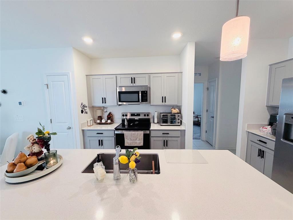 A kitchen features light gray cabinets, white countertops, a central island, and stainless steel appliances — 2715 GENTLE RAIN DRIVE, DAVENPORT, FL
